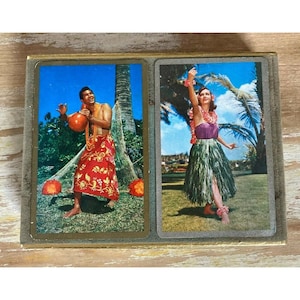 May include: Two rectangular playing cards featuring vintage-style photography. The left card shows a person in a red floral sarong holding a gourd. The right card depicts a person in a purple top and green grass skirt with a floral lei.
