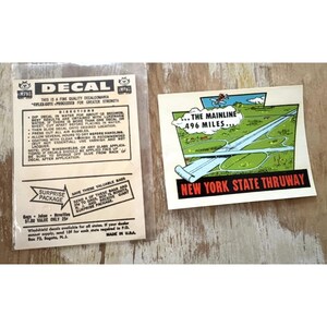May include: A vintage New York State Thruway decal featuring a cartoon illustration of a highway with the text ...THE MAINLINE 496 MILES... and NEW YORK STATE THRUWAY, alongside its original paper packaging with printed instructions and a surprise package offer.