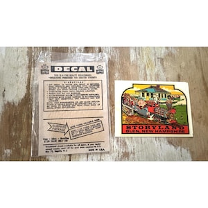 May include: A vintage Storyland Glen, New Hampshire decal featuring a colorful train illustration with passengers, accompanied by a clear plastic bag with printed instructions, directions, and a surprise package offer in black text on a tan background.