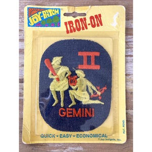 May include: A dark blue oval iron-on patch featuring yellow embroidered figures representing the Gemini zodiac sign, with an orange Roman numeral II, a lyre, and a bow and arrow. The patch is in its original yellow cardboard packaging with the text JOY-PATCH.