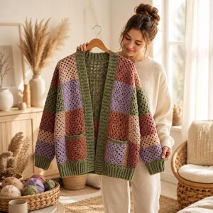 Könnte beinhalten: Eine langärmelige Häkelstrickjacke mit einem Patchwork-Design aus quadratischen Motiven in Salbeigrün, Altrosa, Lavendel und Beige. Das Kleidungsstück hat einen gerippten Saum in Salbeigrün an der Vorderseite, den Ärmelbündchen und am Saum sowie zwei Taschen.