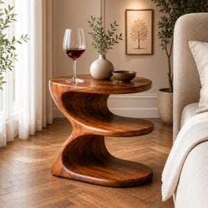 May include: A brown wooden side table with a distinct S-shaped profile featuring three tiered surfaces. The top surface holds a clear glass filled with red wine, a small beige ceramic vase with green sprigs, and a small dark brown bowl.