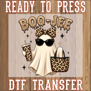 May include: A DTF transfer design featuring a ghost wearing black sunglasses and a leopard print bow. The ghost holds a leopard print tumbler and a matching handbag. The text reads READY TO PRESS at the top and BOO-JEE in gold glitter.