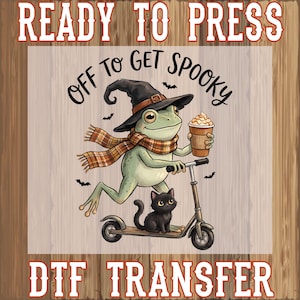 May include: A DTF transfer featuring a green frog wearing a witch hat and a plaid scarf, riding a scooter while holding a coffee cup. A black cat sits on the scooter deck. The text reads READY TO PRESS, OFF TO GET SPOOKY, and DTF TRANSFER.