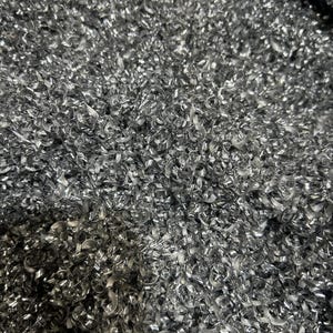 May include: A dense collection of silver-colored metal shavings, characterized by small, tightly coiled, and irregular spiral fragments. The texture is highly reflective and metallic, creating a complex, layered surface of sharp, thin, and twisted steel curls.