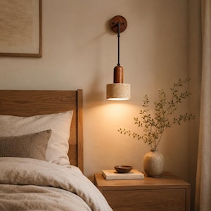 May include: A wall-mounted light fixture featuring a circular dark wood base, a thin black metal rod, a cylindrical wood accent, and a textured beige stone shade. The light emits a warm glow downwards, illuminating the wall and a wooden nightstand.