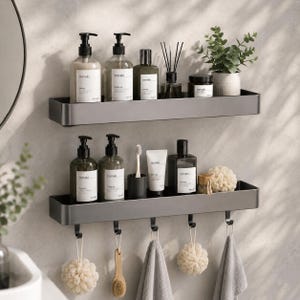 May include: Two matte dark gray rectangular wall shelves with raised edges. The top shelf holds four bottles, a reed diffuser, and a small potted plant. The bottom shelf holds two bottles, a toothbrush holder, a tube, and hanging bath accessories.