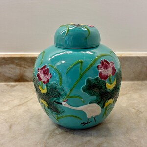 May include: A turquoise ceramic ginger jar with a matching lid, featuring raised relief designs of pink lotus flowers, dark green lily pads, and a white crane with a red crest, all rendered in a glossy finish with vibrant, multi-colored hand-painted details.