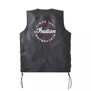 Puede incluir: Un chaleco de cuero negro con cordones laterales y cuerdas colgantes. La parte posterior muestra un logotipo circular con el texto Indian Motorcycle y el año 1901 en bordado blanco y rojo. El chaleco tiene un diseño sin mangas y cuello redondo.