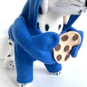 May include: A Dalmatian dog wearing a blue fleece hoodie with a brown felt cookie attached to the paw.