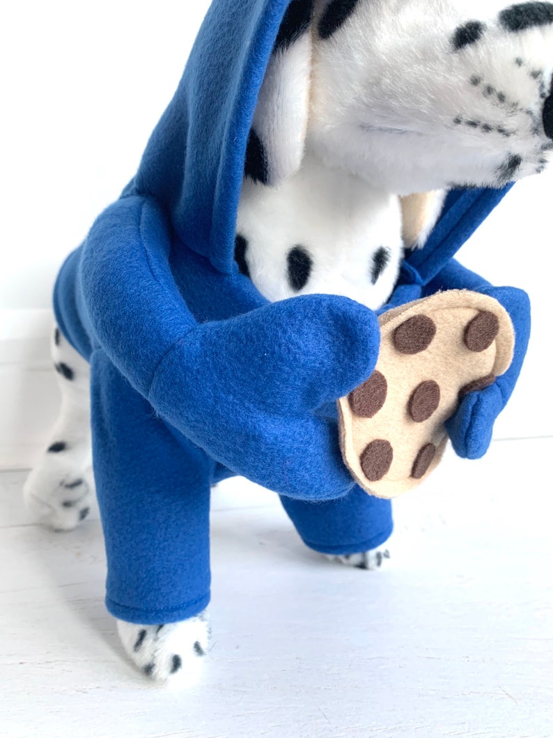 May include: A Dalmatian dog wearing a blue fleece hoodie with a brown felt cookie attached to the paw.