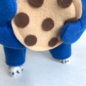 May include: A blue and white dog costume with a large brown and tan felt cookie attached to the front.