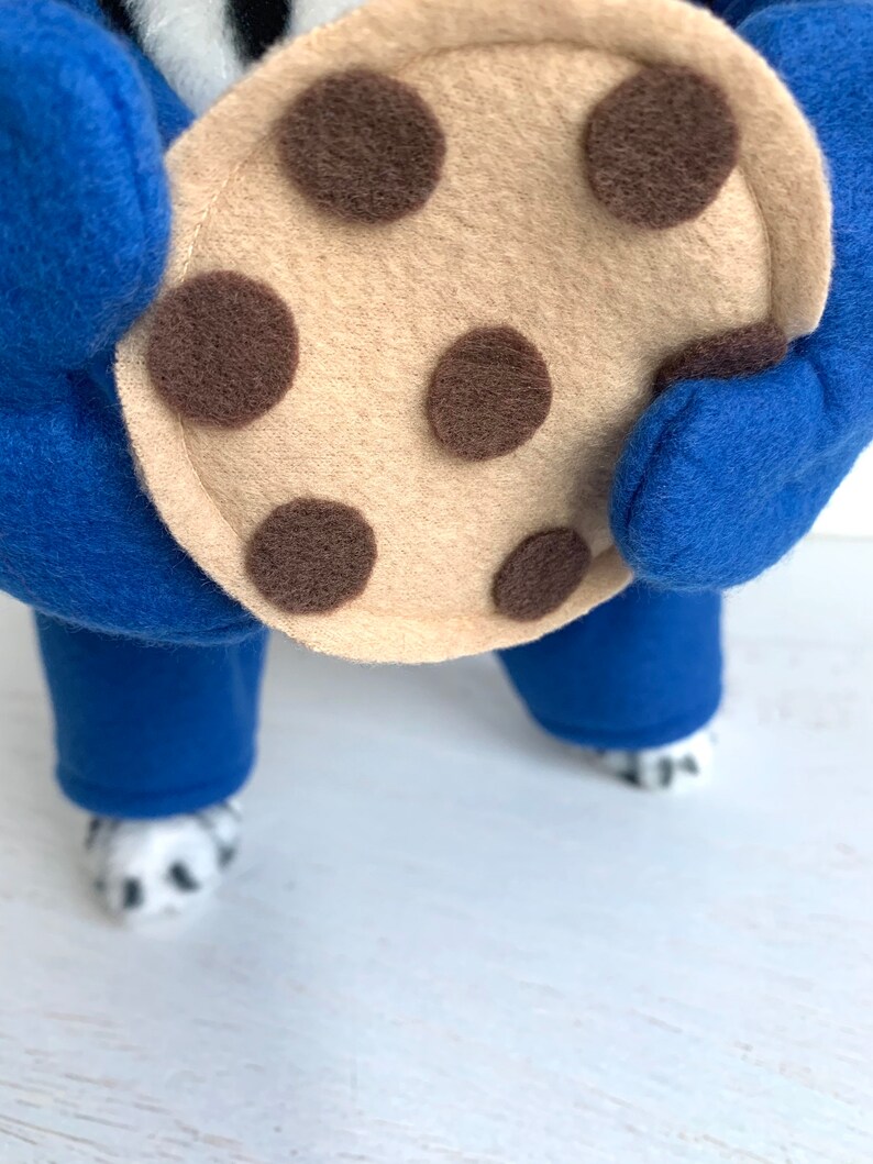 May include: A blue and white dog costume with a large brown and tan felt cookie attached to the front.