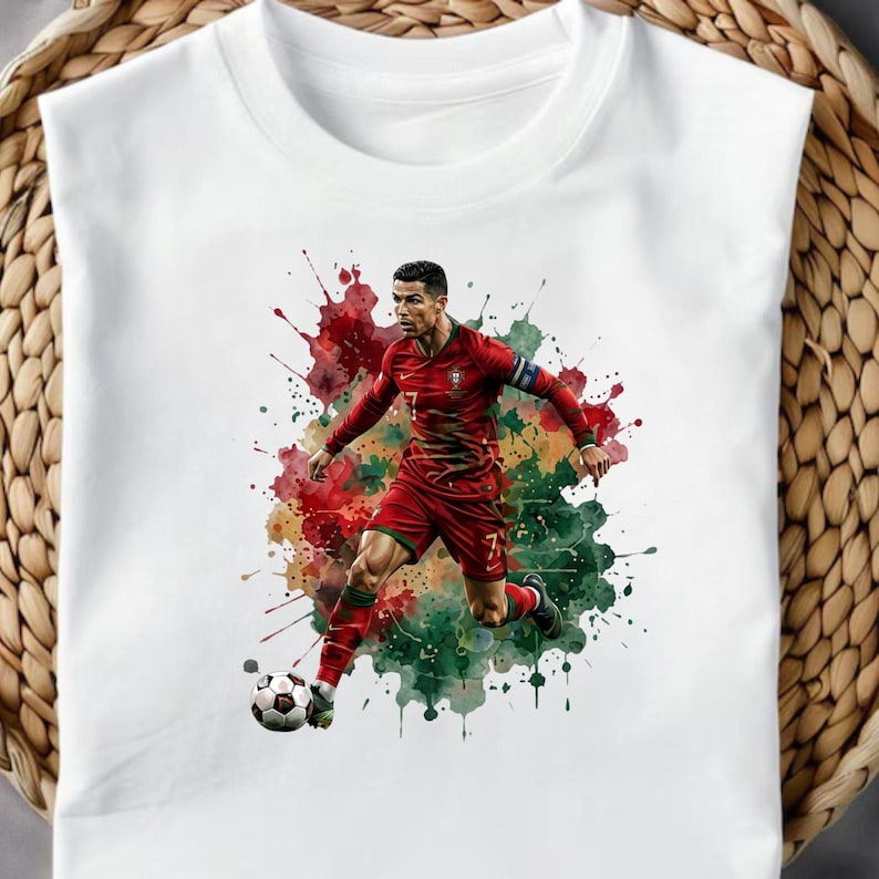May include: A white sleeveless shirt featuring a graphic illustration of a soccer player in a red and green uniform dribbling a soccer ball. The design includes vibrant red and green watercolor-style paint splatters behind the athlete.