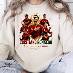 May include: A cream-colored crewneck sweatshirt featuring a graphic print of Cristiano Ronaldo in various poses wearing a red Portugal soccer jersey. The text reads CRISTIANO RONALDO, 6 WORLD CUPS - ONE LEGACY, and Obrigado, Cristiano - CR7.