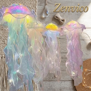 Puede incluir: Tres decoraciones colgantes con forma de medusa iridiscente con tentáculos ondulados translúcidos y luces internas. Las medusas presentan un acabado brillante y multicolor que refleja la luz. El texto Zenvico es visible.