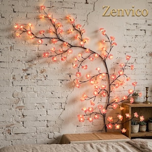 Puede incluir: Una lámpara decorativa de pared con forma de árbol ramificado con numerosas flores de cerezo rosas que se iluminan. Las ramas de color marrón oscuro se extienden sobre una pared de ladrillo blanco y la palabra Zenvico está en dorado.