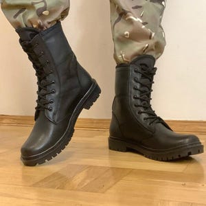 Könnte beinhalten: Ein Paar schwarze Schnürstiefel im Kampfstiefel-Stil mit glatter Oberfläche, hohem Schaft und dicken, profilierten Gummisohlen. Die Stiefel werden mit schwarzen Schnürsenkeln gebunden und haben ein funktionales Design mit verstärkten Nähten.