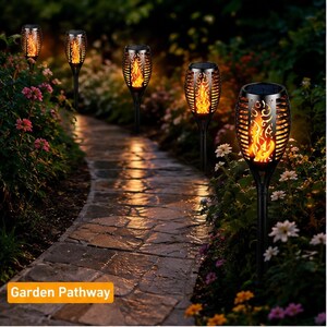 May include: Five black solar-powered garden stake lights with a textured flame-effect design, illuminating a stone pathway. Each light features a solar panel on top and a decorative casing that mimics the appearance of flickering orange flames.