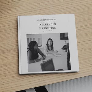 Puede incluir: Un libro cuadrado titulado The Insider's Guide to Influencer Marketing de Katie Stoller. La cubierta blanca presenta una fotografía en blanco y negro de dos personas sentadas en un escritorio con un portátil, sobre una superficie de madera clara.