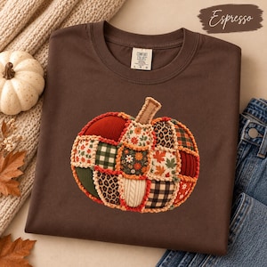 Puede incluir: Una camiseta color marrón espresso con un gráfico central de una calabaza compuesto por varios parches de tela, incluyendo estampados de leopardo, cuadros y flores. La camiseta tiene una etiqueta Comfort Colors en el cuello y es talla L.
