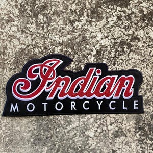 May include: A black embroidered patch featuring the word Indian in a stylized red script font with a white outline, positioned above the word MOTORCYCLE in a clean white sans-serif font, all set against a solid black background fabric.