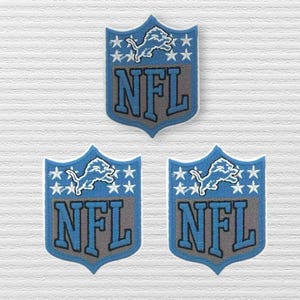 May include: Three embroidered patches shaped like shields, each featuring a light blue lion silhouette above white stars and the letters NFL in dark blue with a grey background, all outlined in white thread on a textured white surface.