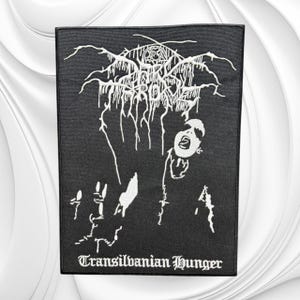 May include: A rectangular black fabric patch featuring a white embroidered graphic design. The top displays the band name Darkthrone in a stylized font, while the bottom features the text Transilvanian Hunger in a gothic typeface.