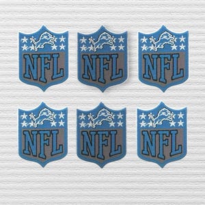 May include: Six shield-shaped patches featuring the Detroit Lions logo in light blue and grey. Each patch displays a leaping lion silhouette above the text NFL, surrounded by small white stars on a light blue background with a grey lower section.