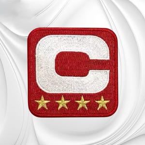 May include: A square embroidered patch with a red background and a large white letter C centered in the upper portion. Below the letter C, there are four small, five-pointed gold stars arranged in a horizontal row across the bottom section.