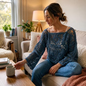 Könnte beinhalten: Ein blauer, langärmeliger Häkelpullover mit quadratischem Ausschnitt und komplizierten, blumenartigen Mustern auf dem Oberteil und den Ärmeln. Das Kleidungsstück besteht aus Garn mit einem sichtbaren Lochmuster und wird mit einer blauen Jeans kombiniert.