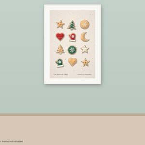 Puede incluir: Una l&aacute;mina de arte mural enmarcada que presenta una cuadr&iacute;cula de doce ilustraciones de galletas con tem&aacute;tica navide&ntilde;a, incluyendo estrellas, &aacute;rboles, corazones, manoplas y una luna creciente. El texto inferior dice THE COOKIE TRAY y baked for december.