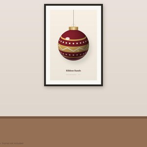 May include: A framed wall art print featuring a dark red Christmas ornament with gold horizontal stripes and white dotted patterns. The ornament hangs from a thin line against a cream background. The text Ribbon Bands is printed below.
