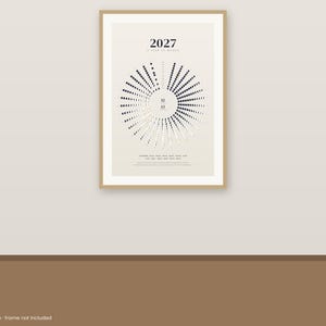 May include: A 2027 wall calendar print featuring a circular lunar phase diagram on a light beige background. The design displays black and white dots arranged in a radial pattern, with the text 2027 A YEAR OF MOONS centered at the top.