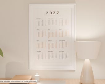 May include: A vertical wall calendar for the year 2027 displayed in a white frame. The calendar features a clean, minimalist layout with the year 2027 at the top, followed by twelve monthly grids arranged in columns, showing dates in black and light text.