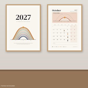 May include: Two framed wall posters featuring a 2027 calendar design. The left poster displays the text 2027 A YEAR OF SUN PATHS above a multi-colored arc graphic. The right poster shows the month of October 2027 with a sun path diagram.
