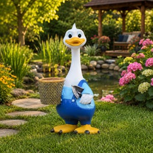 May include: A white goose garden statue wearing blue overalls and yellow feet. The goose has a yellow beak and holds a small, textured, brown woven-style basket in one wing and a small silver-coloured metal hand trowel in the other wing.