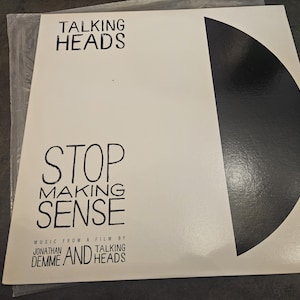 May include: A square vinyl record jacket with a white background and a large black semi-circle on the right side. The text reads Talking Heads Stop Making Sense Music From A Film By Jonathan Demme And Talking Heads in black lettering.
