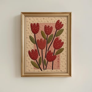 May include: A framed fabric wall hanging featuring a quilted cream background with a central pink rectangle. The design displays red patterned tulip flowers with green leaves and stems. The word PARIS is embroidered vertically in brown thread.