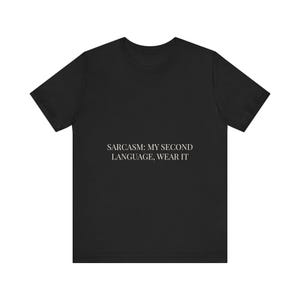 May include: A black short-sleeved t-shirt featuring white text centred on the chest that reads: SARCASM: MY SECOND LANGUAGE, WEAR IT. The garment has a crew neckline and a standard fit, constructed from a solid-coloured fabric with a clean design.