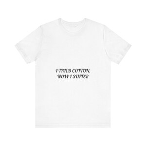 以下が含まれることがあります： 中央に黒いイタリック体のセリフフォントで「I TRIED COTTON, NOW I SUFFER」というテキストがプリントされた、白い半袖Tシャツ。この衣類は、クラシックなクルーネックと標準的な半袖のデザインが特徴です。