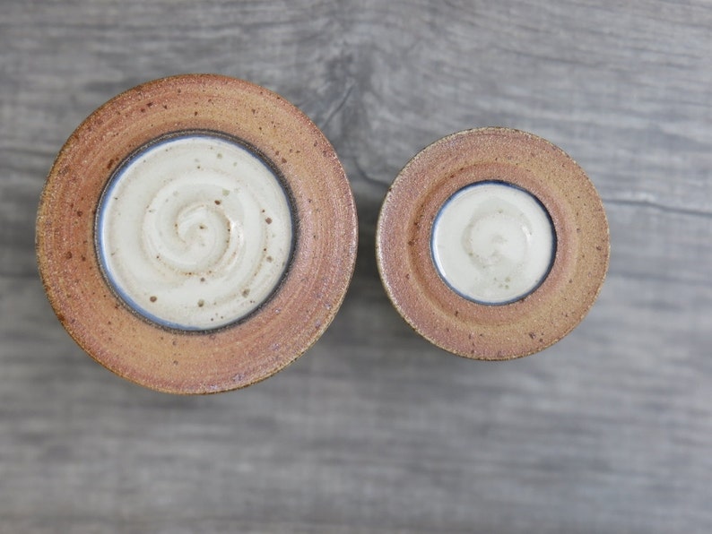 May include: Two ceramic bowls with a brown glaze and a white interior. The larger bowl has a swirl design in the center. The smaller bowl has a plain white interior.