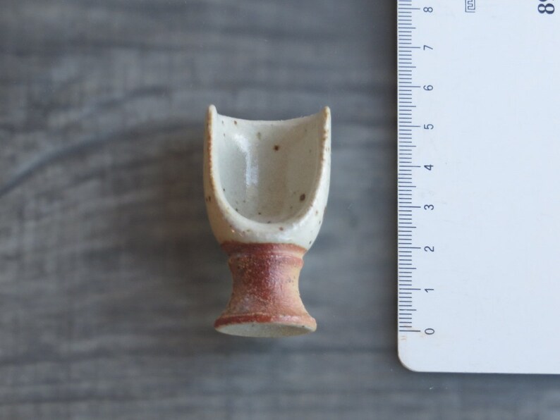 May include: A small, white ceramic cup with a brown base. The cup is designed to hold a single serving of something, like a teacup.