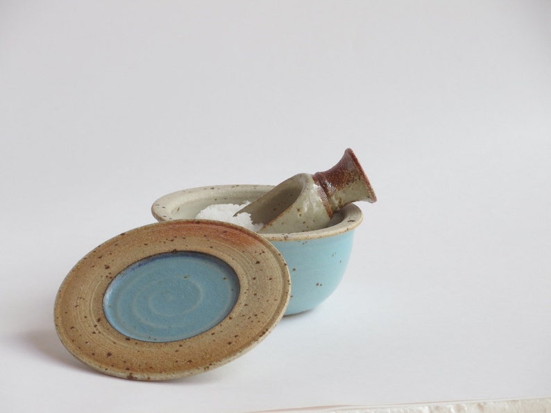 May include: A blue ceramic salt cellar with a lid and a small scoop. The cellar is filled with white salt.