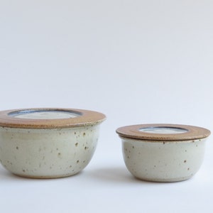 May include: Two ceramic butter dishes with lids. The larger dish is off-white with brown speckles and a brown lid. The smaller dish is the same color and has a brown lid.
