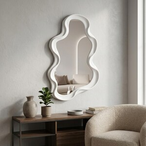 May include: A wall-mounted mirror featuring an irregular, wavy, organic-shaped white frame. The reflective glass surface displays a clear view of a room interior, capturing the light and depth of the space within its smooth, curved border.