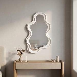 May include: A wall-mounted mirror featuring an irregular, wavy, organic-shaped frame in a solid matte white finish. The reflective glass surface is encased within the thick, smooth, undulating border, creating a fluid and asymmetrical silhouette.