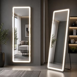 Puede incluir: Dos espejos rectangulares de cuerpo entero con esquinas redondeadas y tiras de luz LED integradas a lo largo del marco interior. Un espejo está montado contra una pared gris, mientras que el otro se apoya en ángulo sobre un soporte de metal negro.
