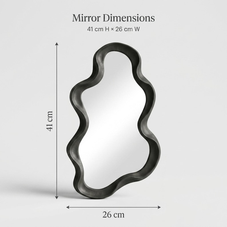 May include: An irregular, wavy-shaped mirror with a thick black frame. Text at the top reads Mirror Dimensions 41 cm H x 26 cm W. Arrows indicate the height of 41 cm and width of 26 cm, showing the mirror is approximately 16.14 inches by 10.24 inches.