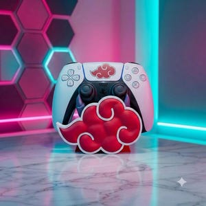 Puede incluir: Un mando de videojuegos blanco y negro con un emblema de nube roja y blanca en el panel táctil central. El mando descansa sobre un soporte rojo con forma de nube que coincide con el diseño del emblema, creando un conjunto de accesorios.